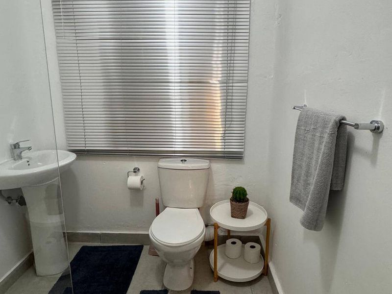 A functional bathroom featuring a pedestal sink, standard toilet, tiled flooring, and a window fitted with horizontal blinds.