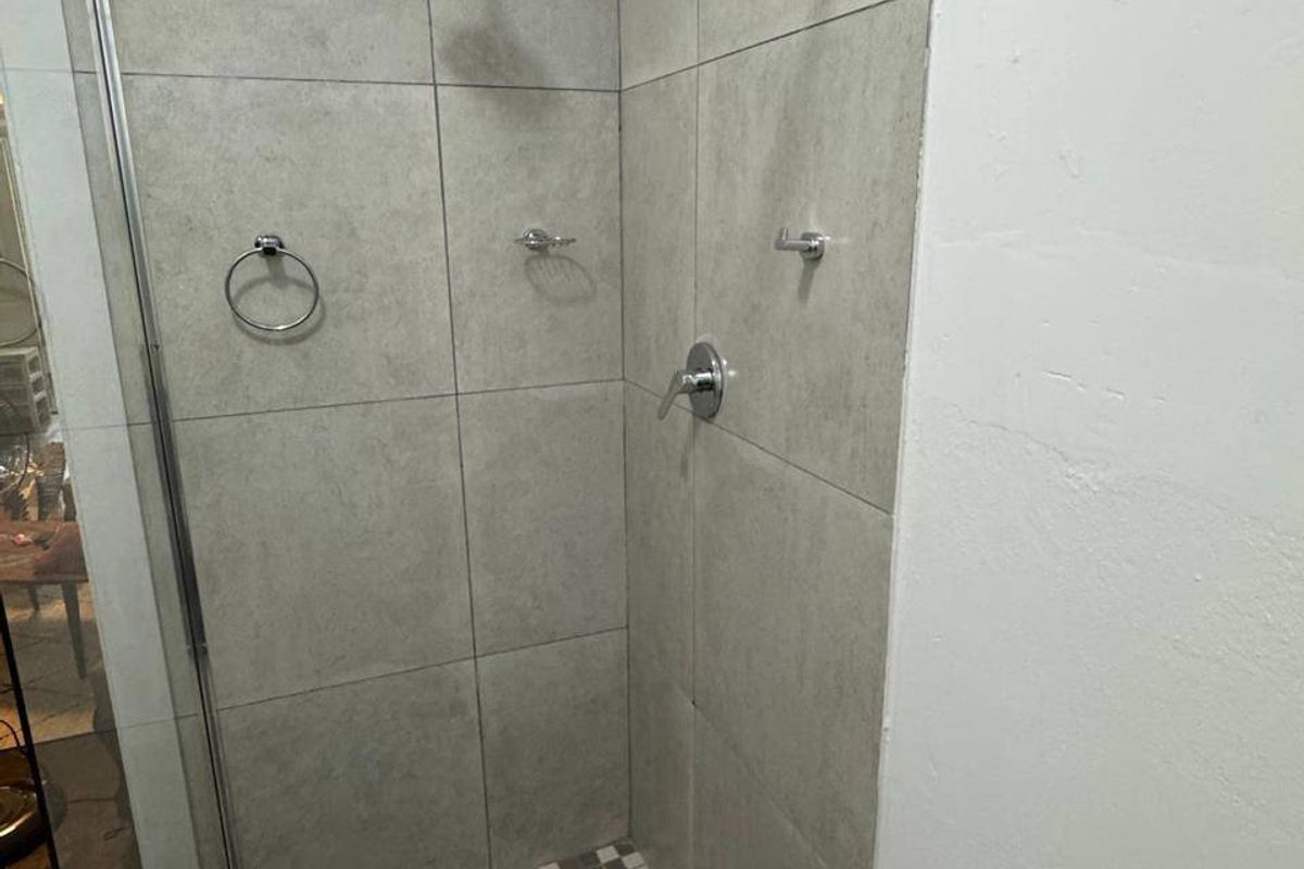 A modern walk-in shower featuring large format grey wall tiles, a mosaic tiled floor, and chrome shower fixtures with a glass enclosure.