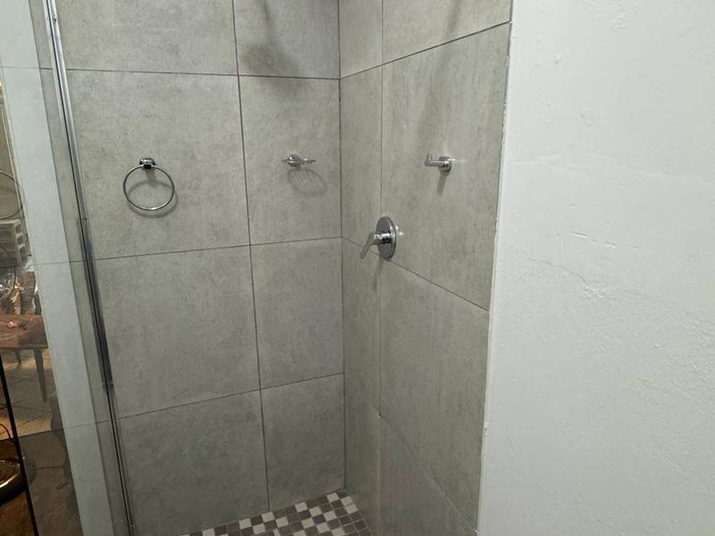 A modern walk-in shower featuring large format grey wall tiles, a mosaic tiled floor, and chrome shower fixtures with a glass enclosure.