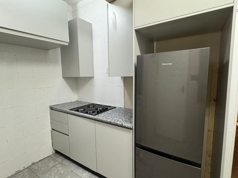 Compact kitchen featuring grey cabinetry, granite-look countertops, and a built-in electric hob, with space for a refrigerator.