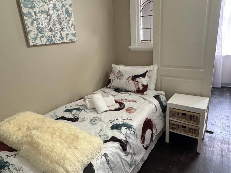 A compact bedroom featuring dark wood-look flooring, a leaded glass window, and a classic panel door.
