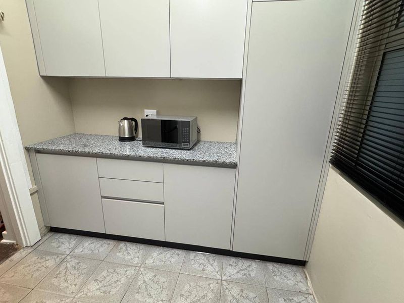 A functional kitchen area featuring light grey cabinetry, granite-look countertops, and tiled flooring, providing efficient storage and workspace.