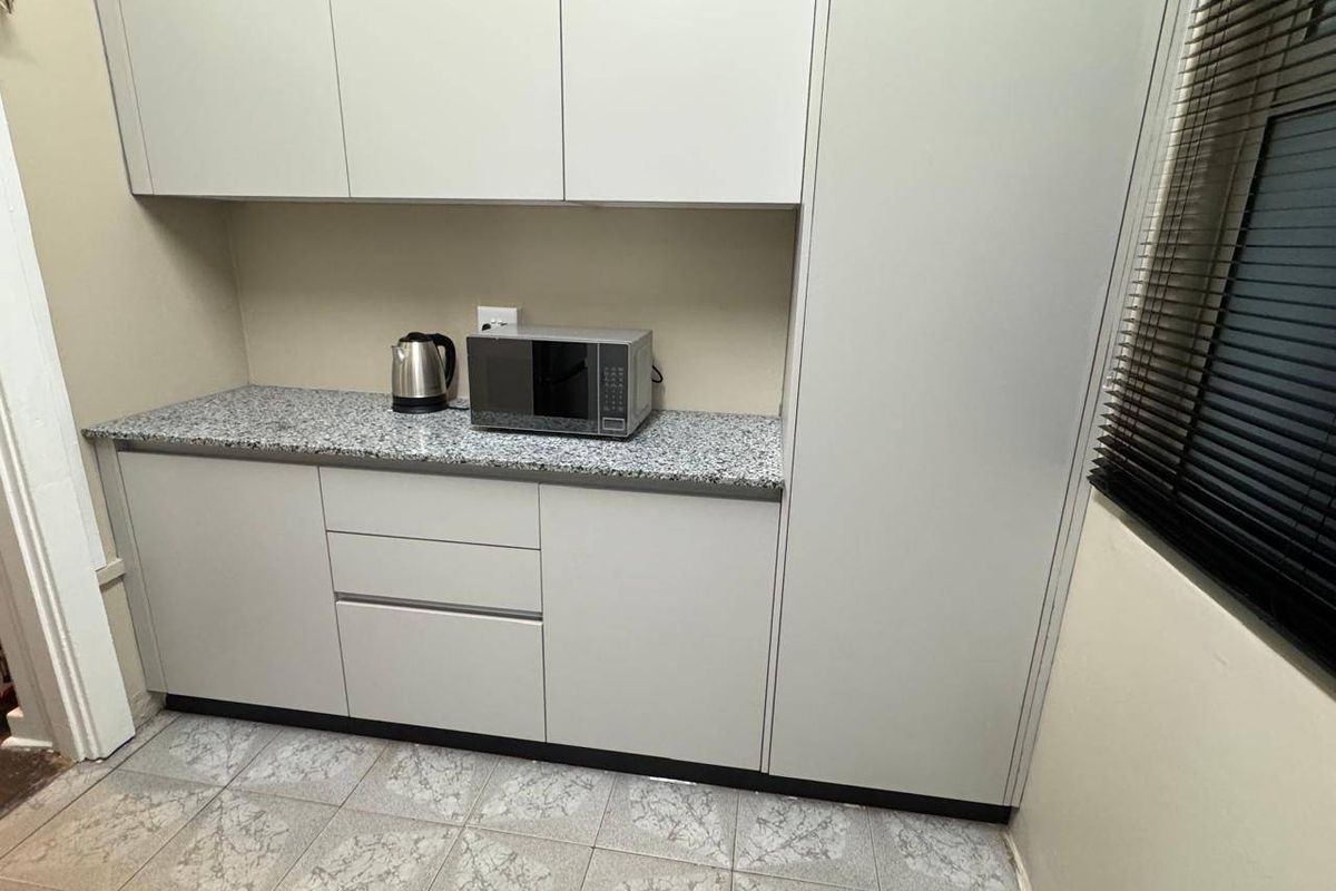 A functional kitchen area featuring light grey cabinetry, granite-look countertops, and tiled flooring, providing efficient storage and workspace.