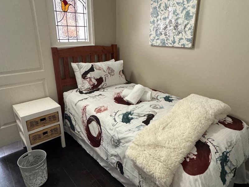A compact bedroom featuring dark timber flooring and a decorative stained glass window.