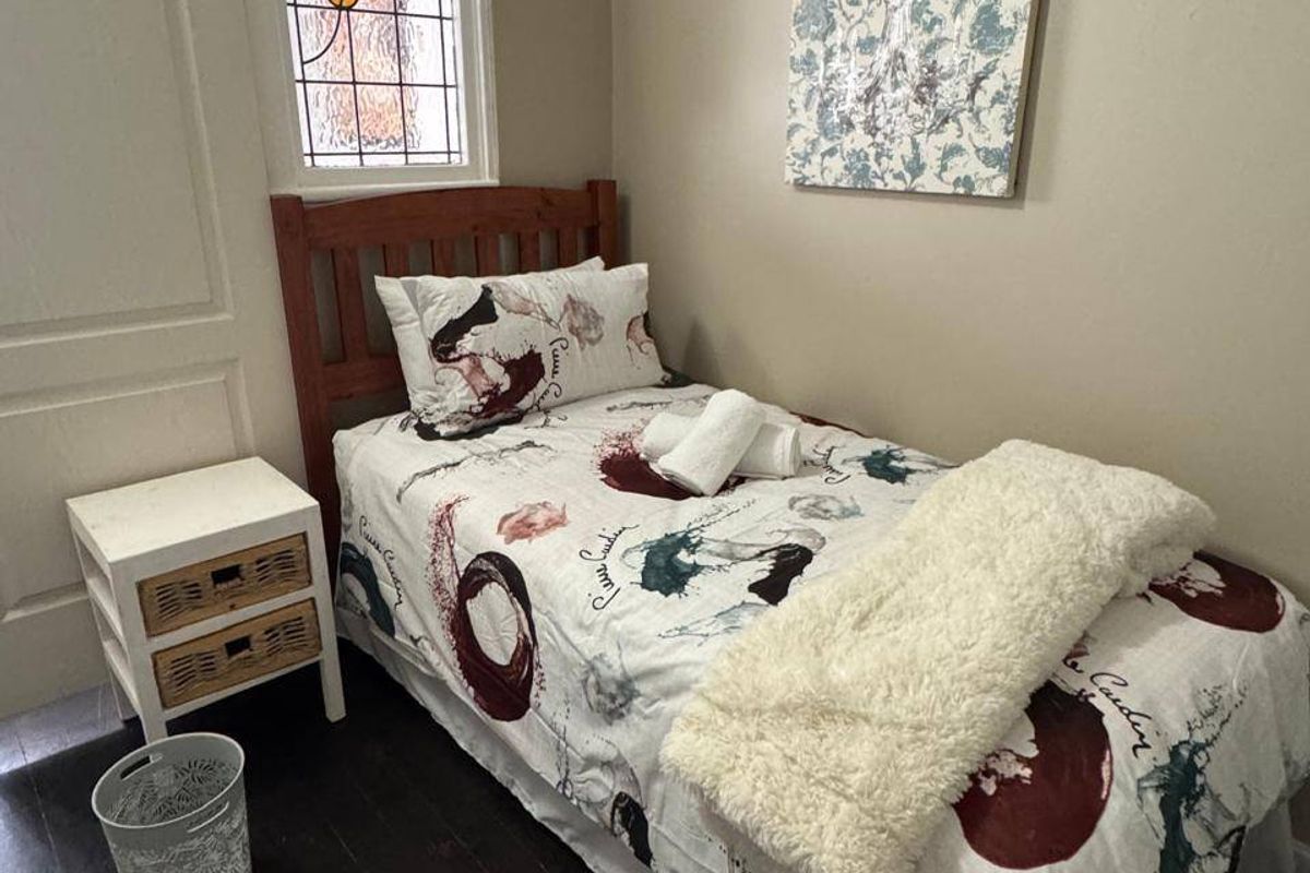 A compact bedroom featuring dark timber flooring and a decorative stained glass window.