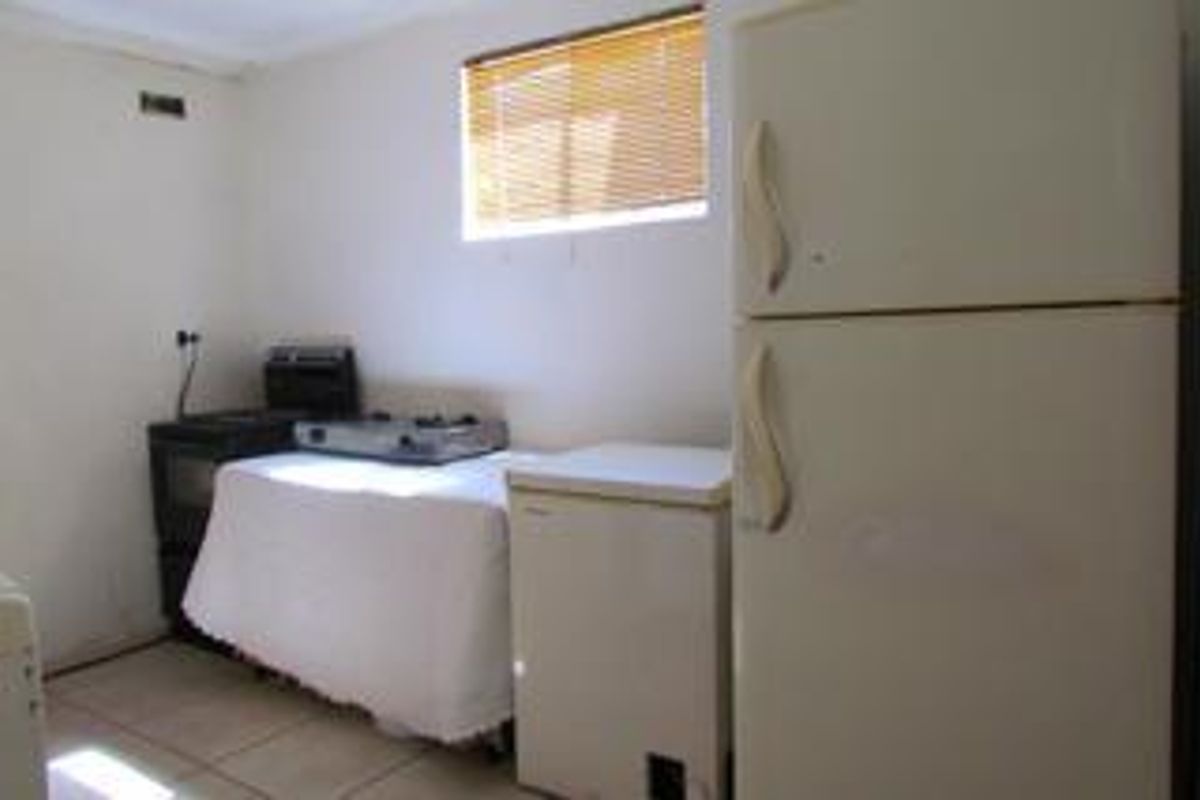 A functional kitchen area featuring tiled flooring and a window with venetian blinds, providing a basic space for food preparation and storage.