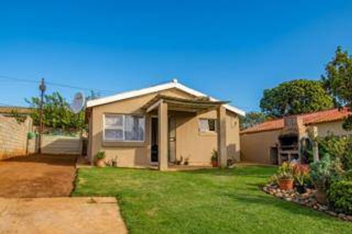 Rear view of the property featuring a covered patio, a built-in braai area, and a well-maintained garden space.