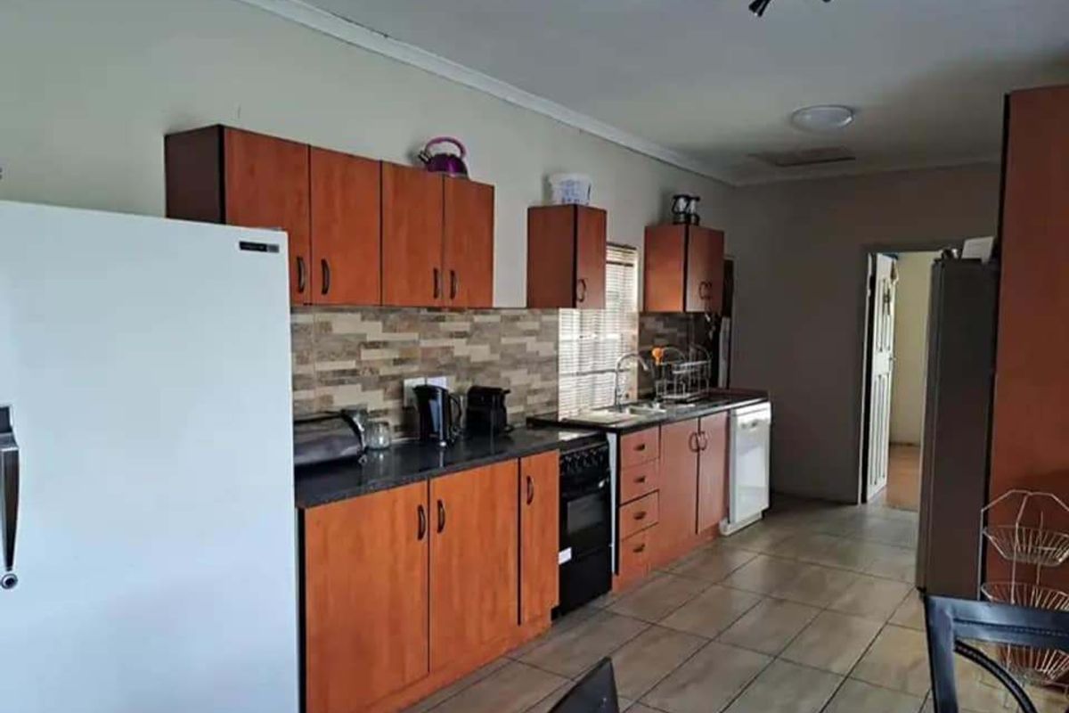 A functional kitchen featuring wood-finish cabinetry, stone-look countertops, tiled backsplash, and ceramic floor tiles, providing a practical workspace with integrated storage.