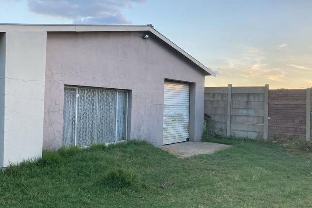 Rear view of the property featuring a roller garage door, security bars on windows, and a precast concrete boundary wall.