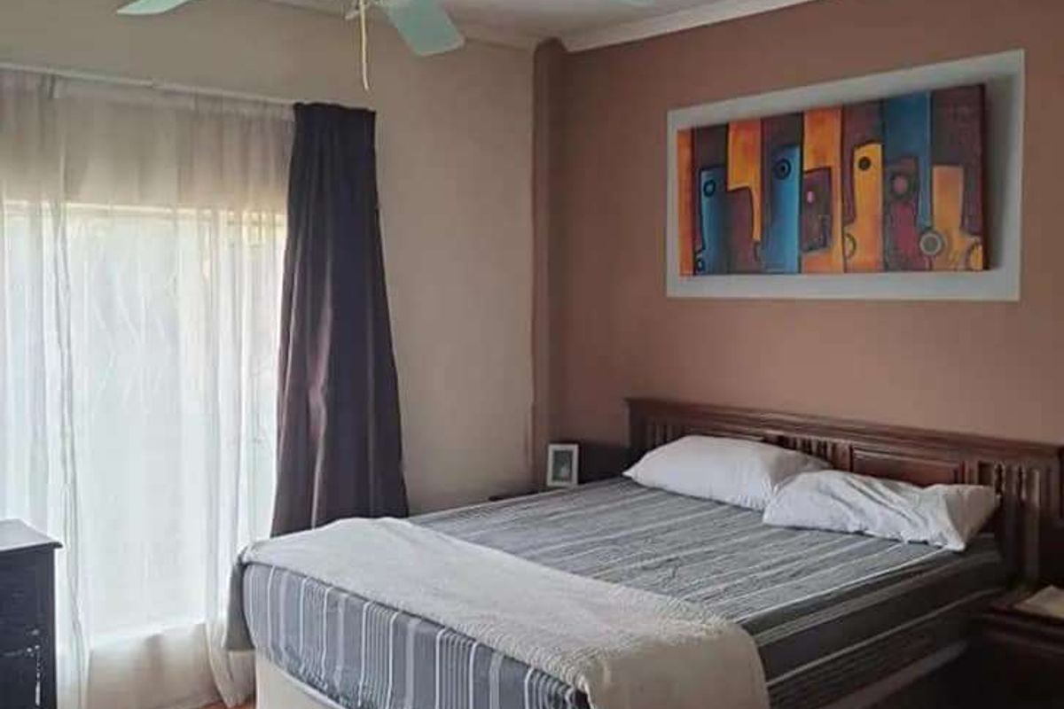 A bedroom featuring laminate flooring and a ceiling fan, with a neutral color palette and natural light from the window.