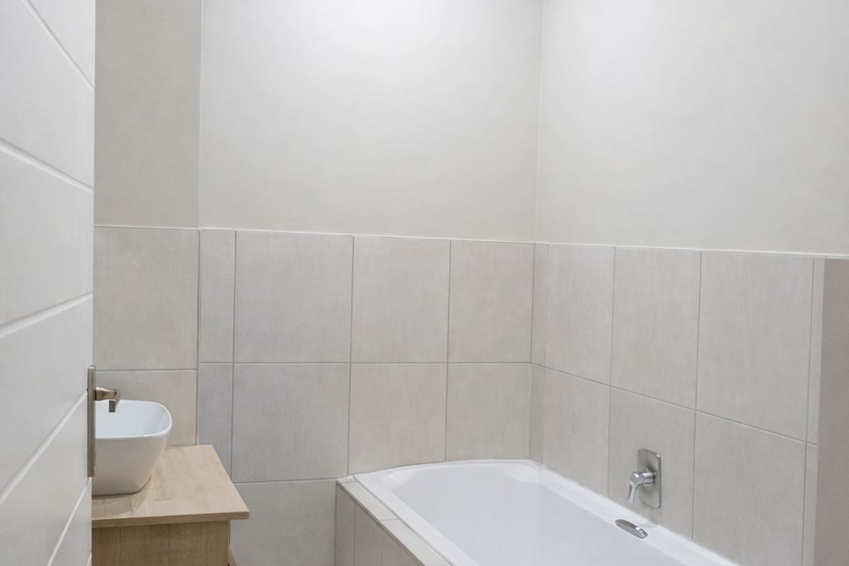 A modern bathroom featuring a built-in bathtub, a wooden vanity with a vessel sink, and neutral wall and floor tiling.