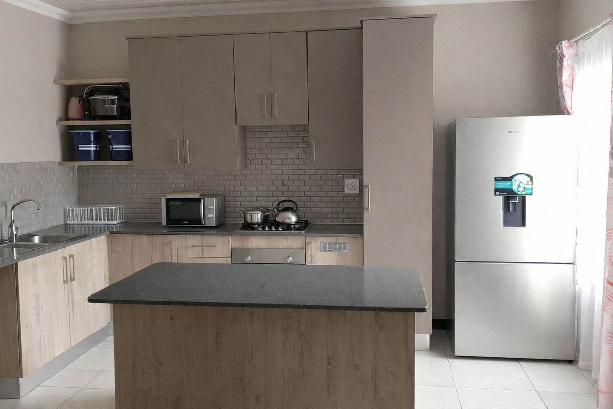 Modern kitchen featuring light wood-tone cabinetry, subway tile backsplash, stone-look countertops, a central island, and integrated stainless steel appliances.