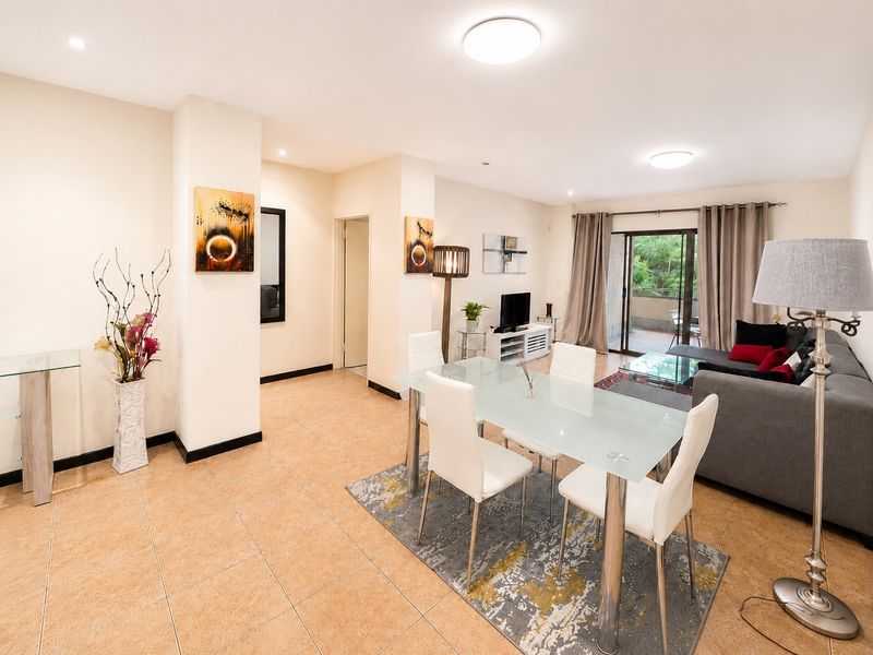 Spacious open-plan living and dining area featuring neutral tiled flooring, recessed lighting, and direct access to a private balcony through sliding glass doors.
