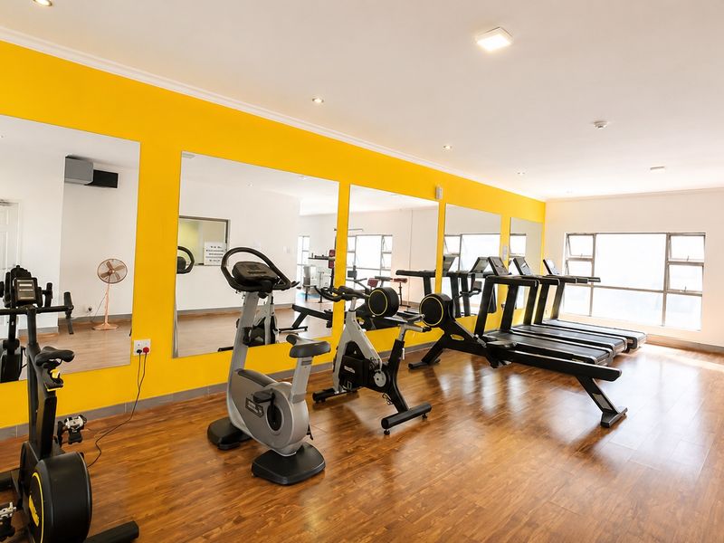 A well-lit gym facility featuring large wall-mounted mirrors, laminate flooring, and aluminium-framed windows, providing a functional space for exercise.