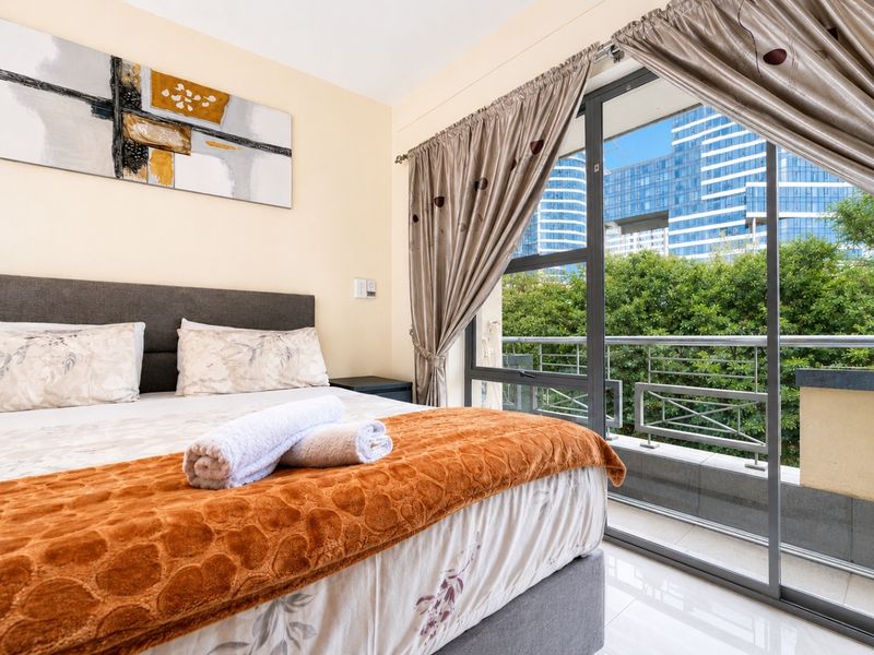 A well-lit bedroom featuring tiled flooring and a large sliding glass door that opens onto a private balcony with urban views.