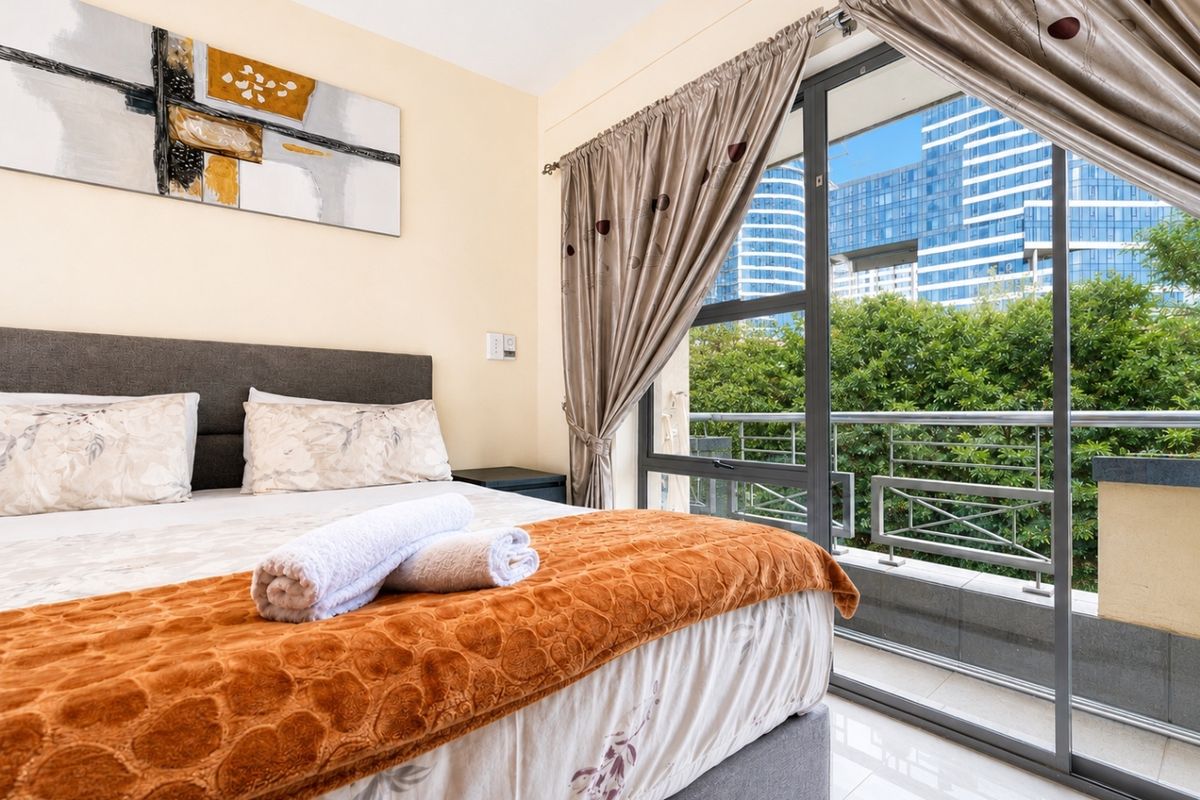 A well-lit bedroom featuring tiled flooring and a large sliding glass door that opens onto a private balcony with urban views.