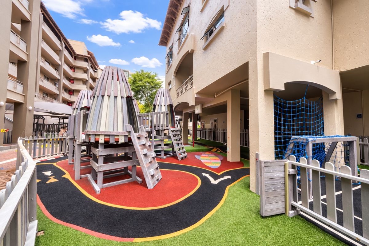 A well-maintained communal playground area located within the apartment complex, featuring rubberized safety flooring and integrated climbing structures.