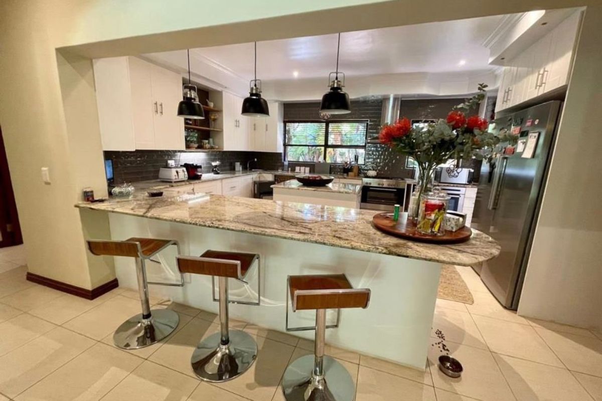 A well-appointed kitchen featuring a large granite-topped island with breakfast bar seating, modern pendant lighting, and ample built-in cabinetry.
