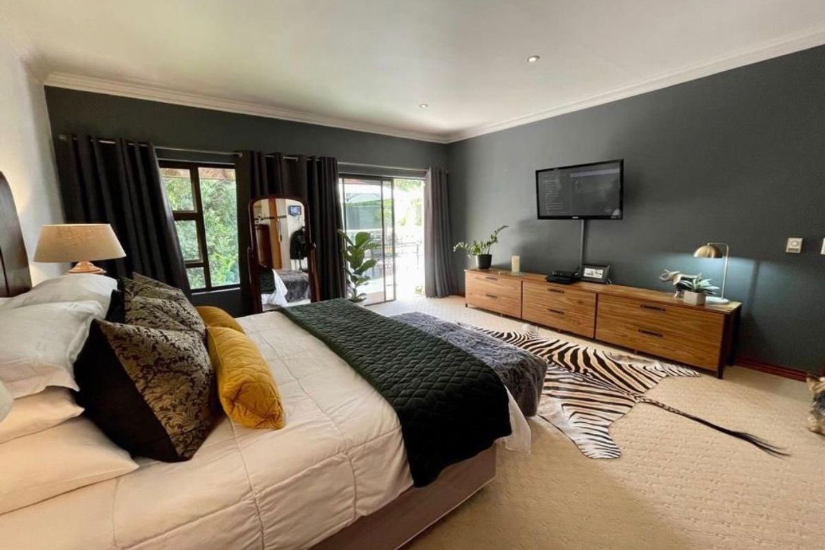 Spacious bedroom featuring dark accent walls, recessed downlighting, and sliding glass doors providing access to the exterior.