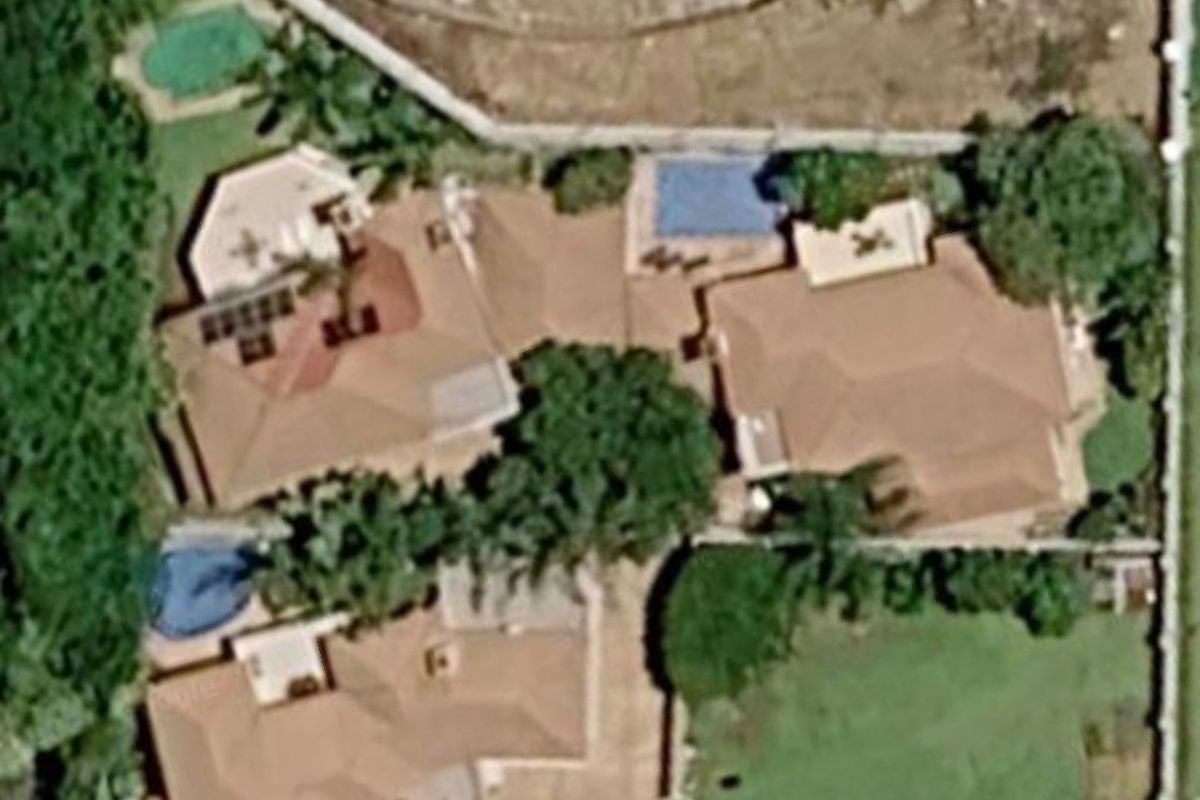 Aerial view of the property showing the main dwelling, multiple roof sections, swimming pool, paved areas, and surrounding garden space.