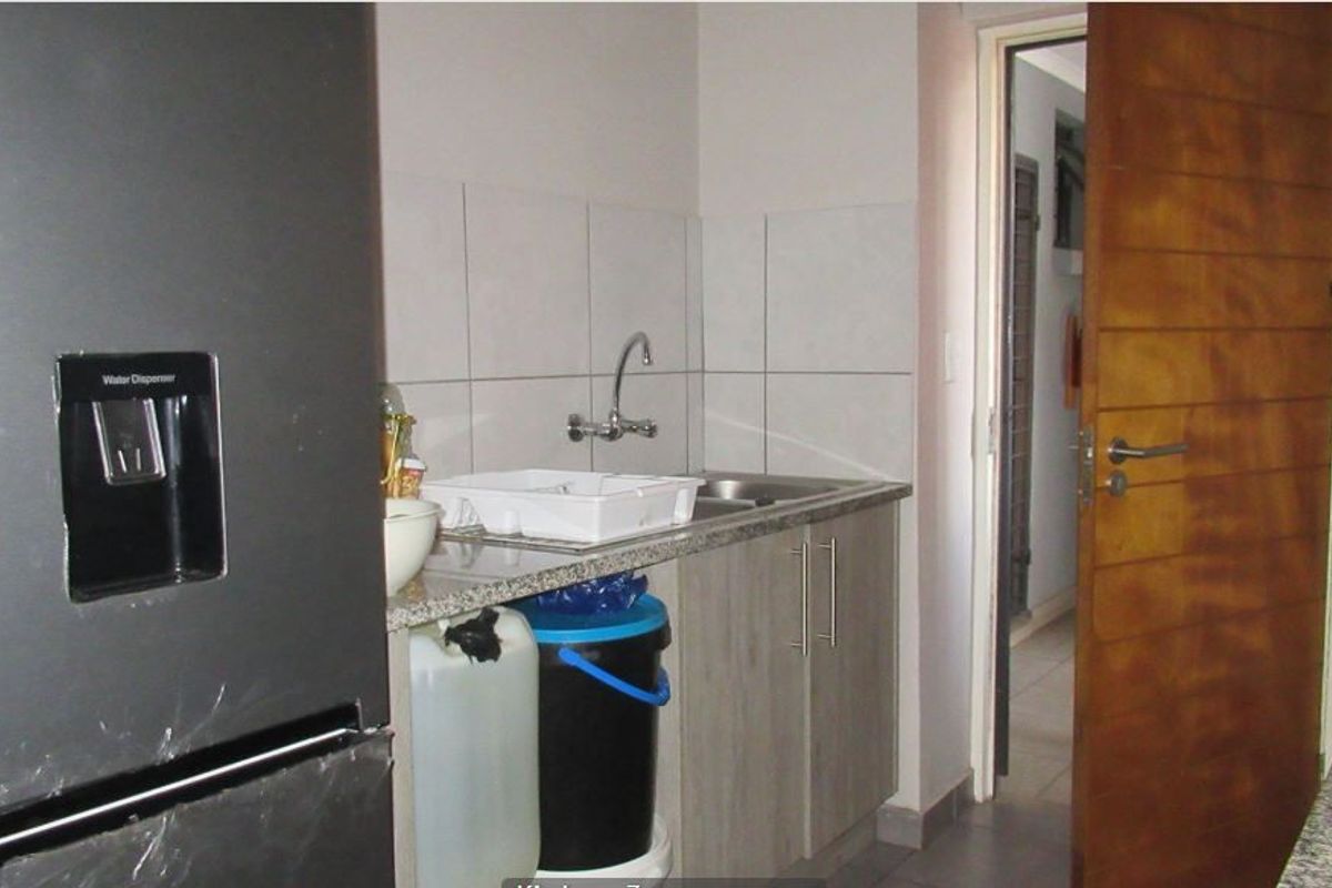 A compact kitchen area featuring granite countertops, a stainless steel sink, tiled backsplash, and light-toned laminate cabinetry.
