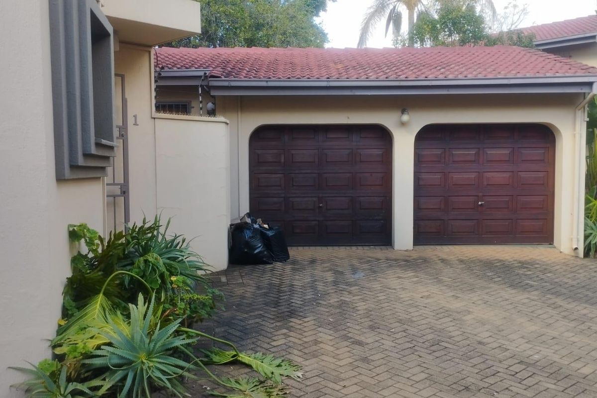 Front exterior view of the townhouse featuring a double garage with wooden doors and a paved driveway.