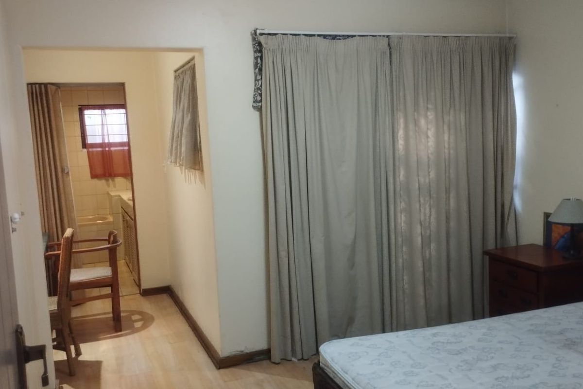 A bedroom featuring laminate flooring and curtain tracks, with an adjoining bathroom visible through the doorway.