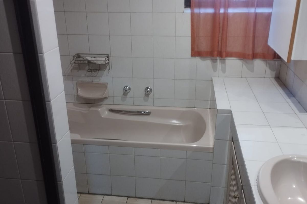 A functional bathroom featuring a built-in bathtub, tiled vanity countertop with a drop-in basin, and classic wall tiling.