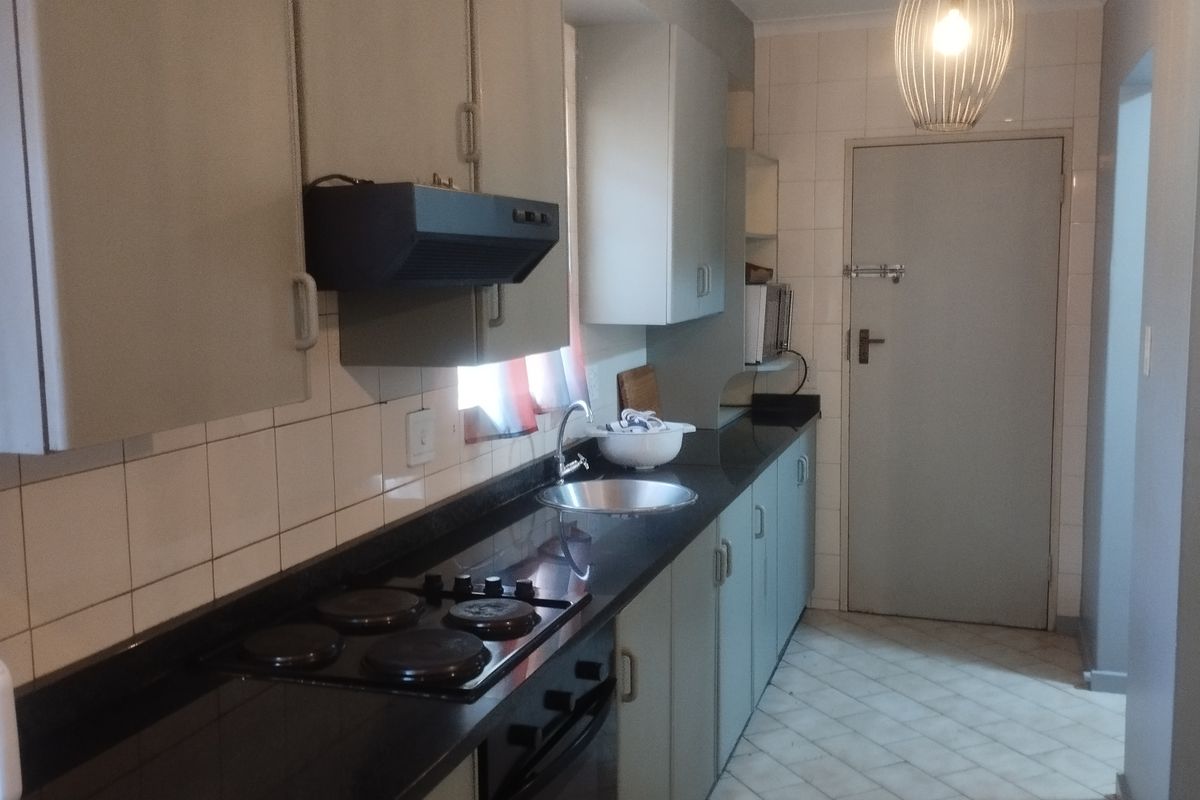 Functional kitchen featuring built-in cabinetry, black granite countertops, an electric hob, oven, extractor fan, and tiled finishes.