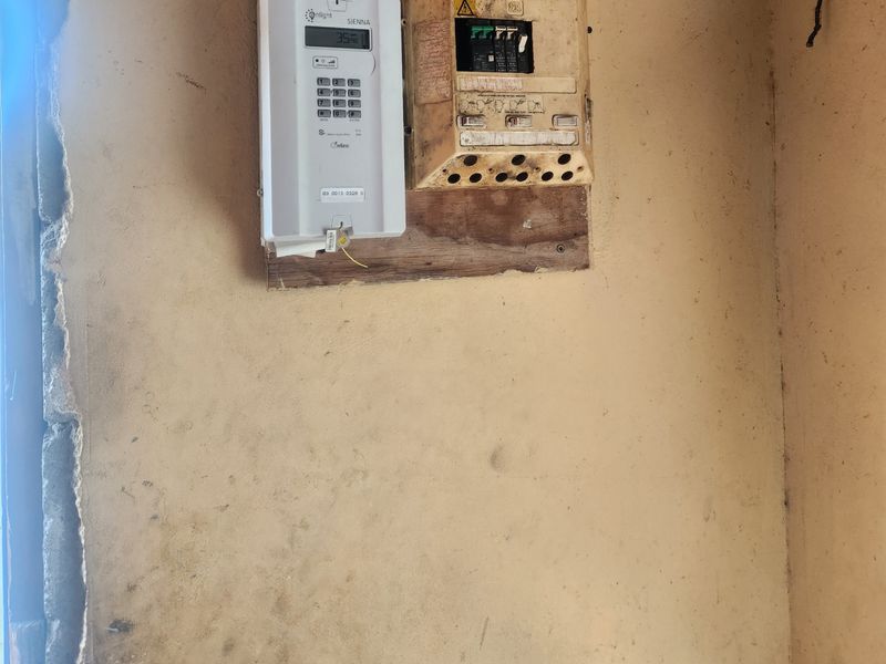 Utility area featuring a wall-mounted prepaid electricity meter and electrical distribution board with visible signs of wall damage and wear.