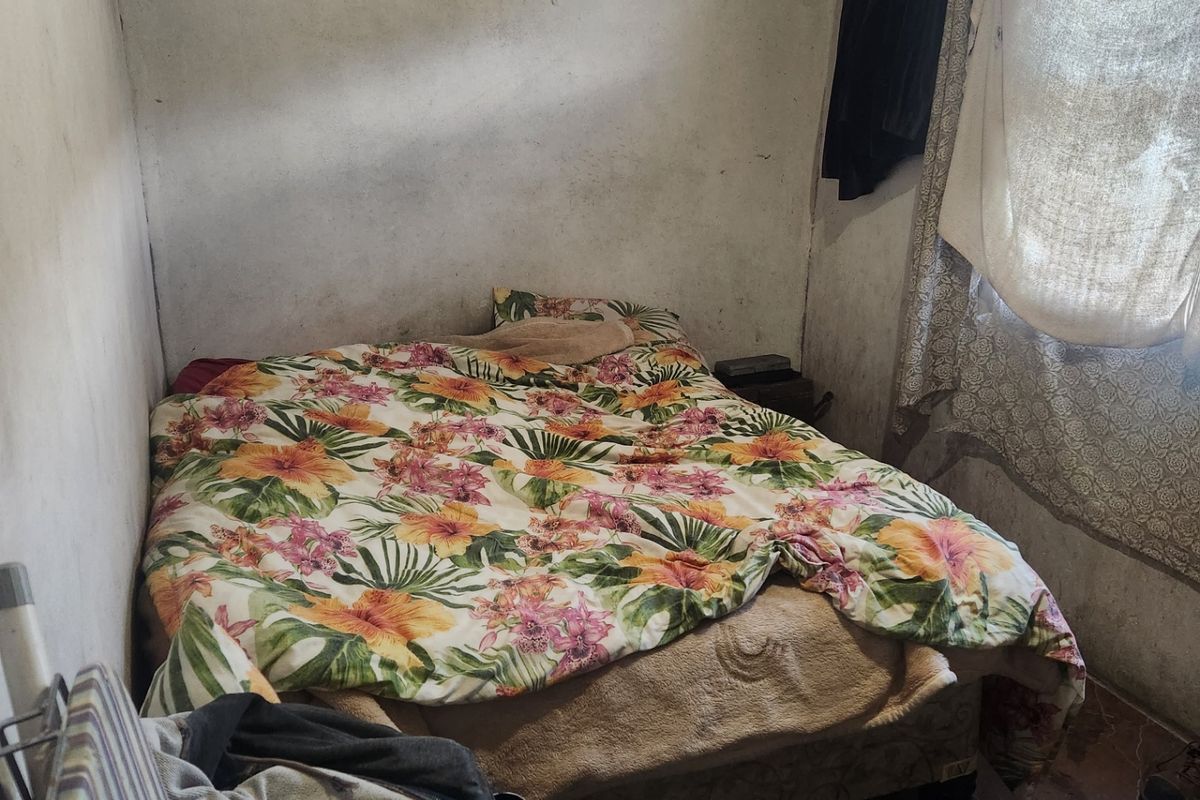 A small bedroom featuring tiled flooring and a window, currently requiring significant cosmetic updates and wall repairs to improve the overall condition.