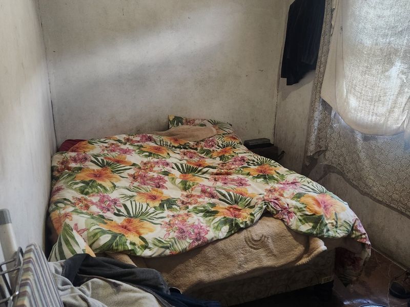 A small bedroom featuring tiled flooring and a window, currently requiring significant cosmetic updates and wall repairs to improve the overall condition.