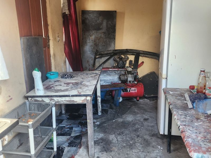 A utility space showing significant wear and tear, featuring tiled flooring and a timber door, requiring substantial renovation and surface repairs.