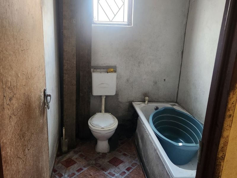 A small, dated bathroom featuring a standard toilet, bathtub, and tiled flooring, requiring significant renovation and cosmetic updates.