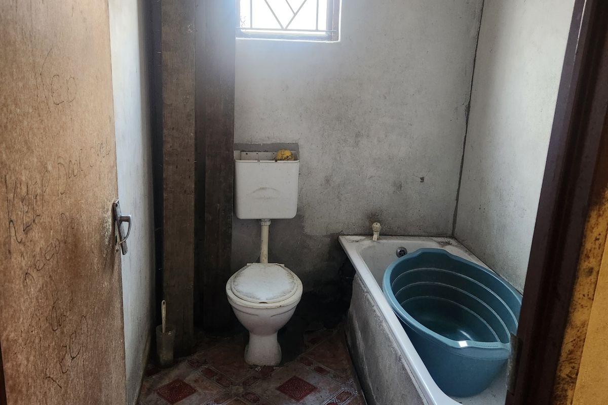 A small, dated bathroom featuring a standard toilet, bathtub, and tiled flooring, requiring significant renovation and cosmetic updates.