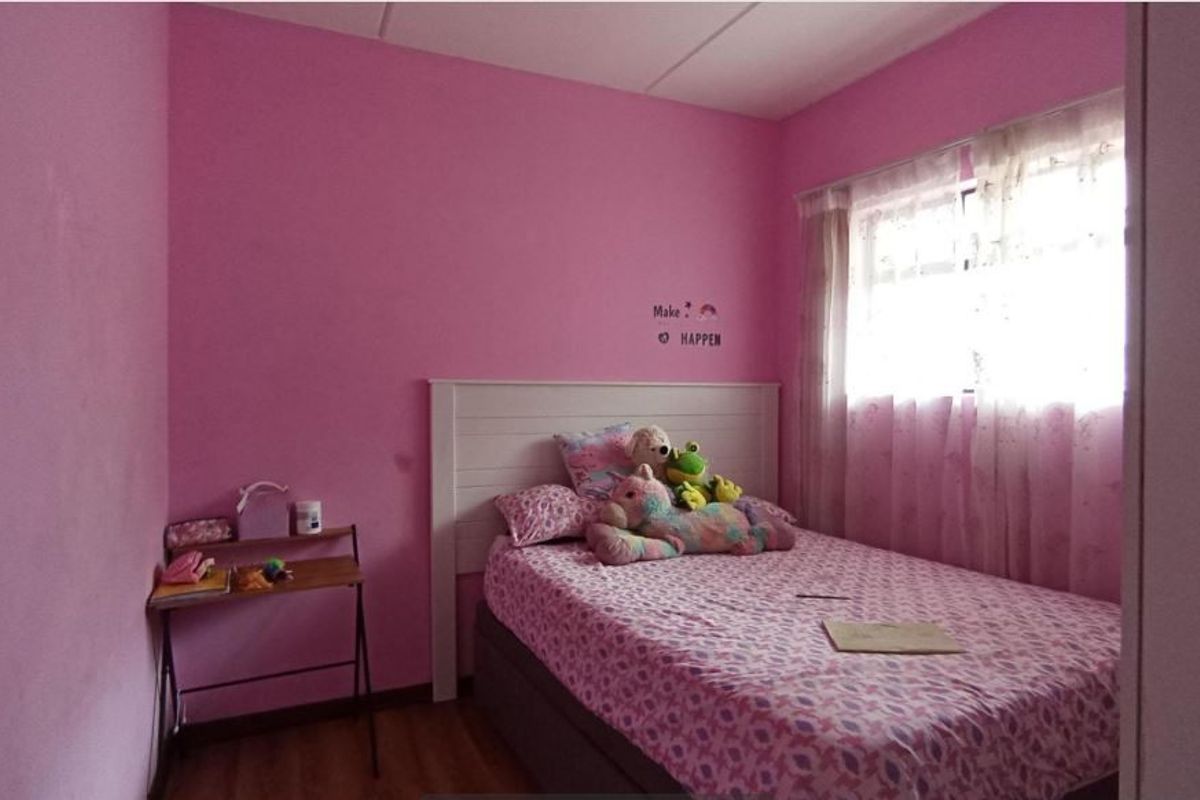 A bedroom featuring pink painted walls and laminate flooring, providing a functional space with natural light from the window.