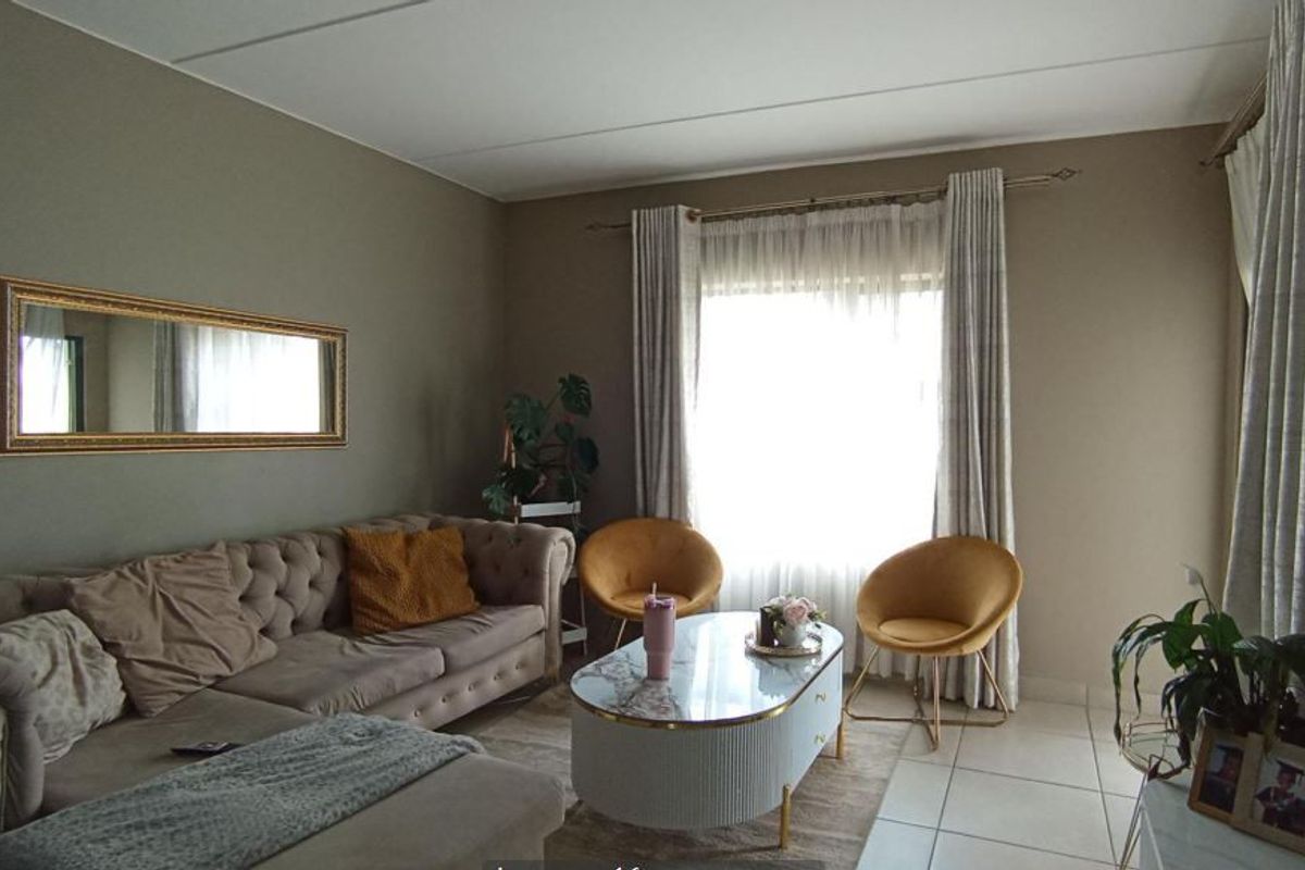 A comfortable living room featuring neutral wall tones, tiled flooring, and large windows with installed curtain tracks for natural light.