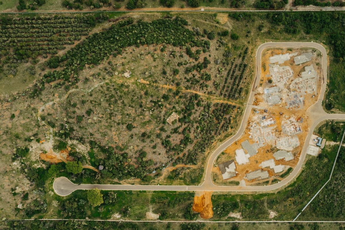 An aerial view of a residential development site showing paved roads, cleared building plots, and surrounding natural vegetation.