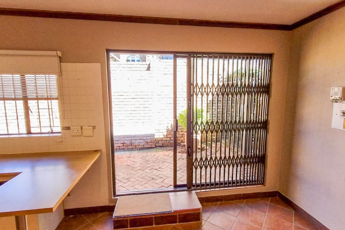 A functional kitchen area featuring tiled flooring, built-in countertops, and a sliding glass door providing direct access to a paved outdoor patio space.