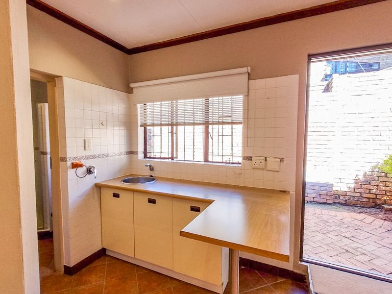 A functional scullery area featuring built-in cabinetry, a stainless steel sink, and direct access to an outdoor paved courtyard.