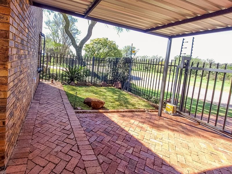 A covered patio area featuring brick paving, metal roofing, and secure perimeter fencing with an integrated sliding gate.
