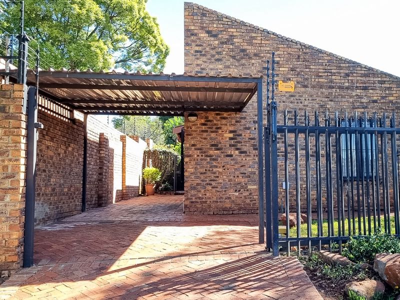 Front exterior view of a townhouse featuring a face brick facade, a covered carport, and secure perimeter fencing with a steel gate.