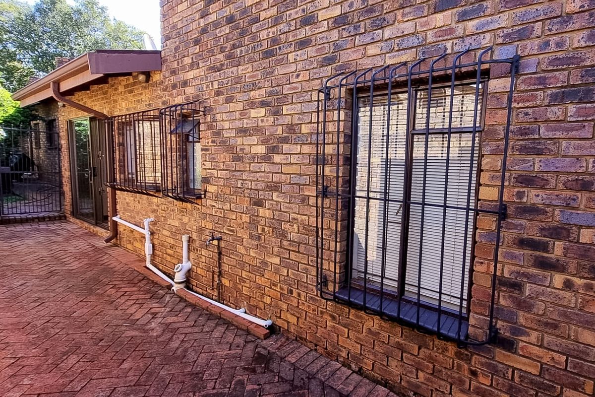 Rear exterior view of the townhouse featuring face brick walls, security bars on windows, and a paved patio area with visible external plumbing.