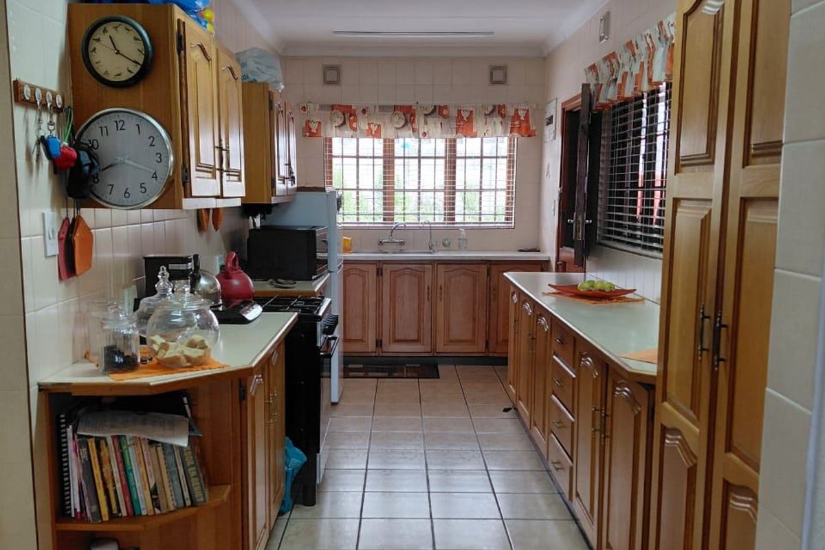 A functional galley-style kitchen featuring extensive wooden cabinetry, tiled flooring, and a double sink, offering ample storage and workspace.