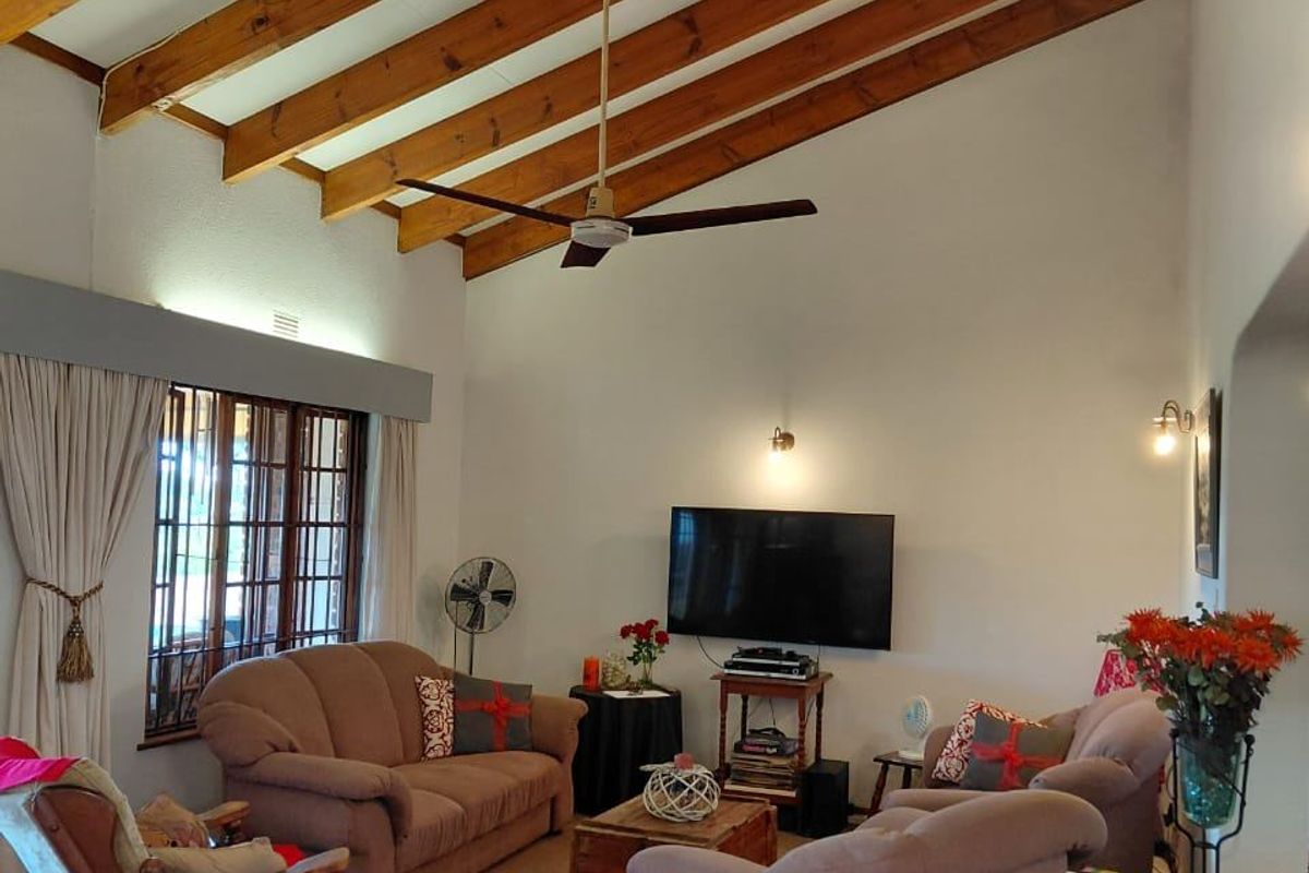 Spacious living room featuring a high vaulted ceiling with exposed timber beams, a ceiling fan, and large timber-framed windows.