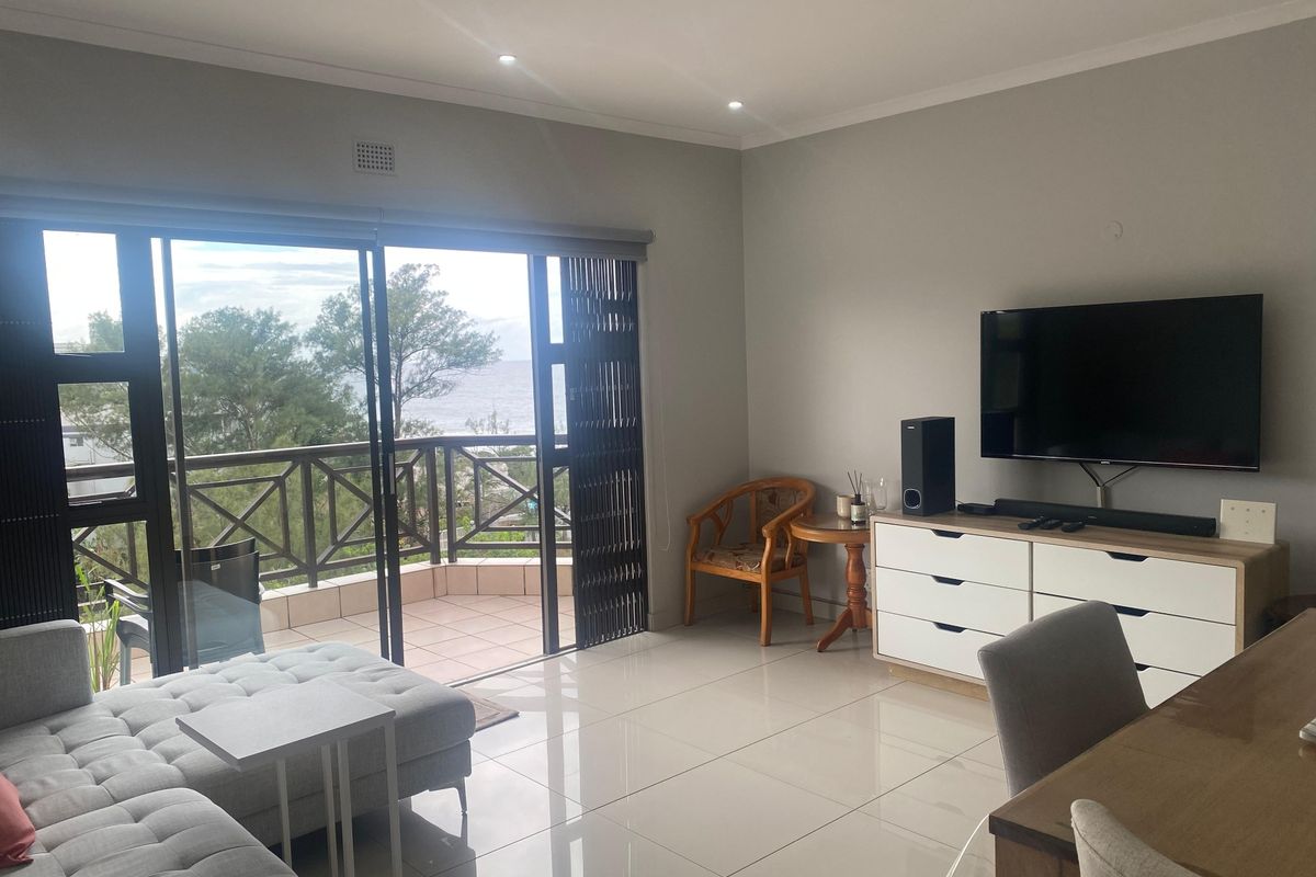 Bright living room featuring large sliding glass doors that open onto a balcony with scenic views and polished tiled flooring throughout.