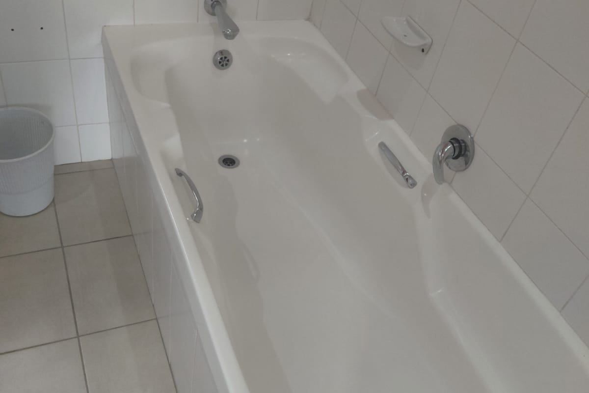A functional bathroom featuring a built-in bathtub with chrome fixtures and neutral ceramic wall and floor tiling.