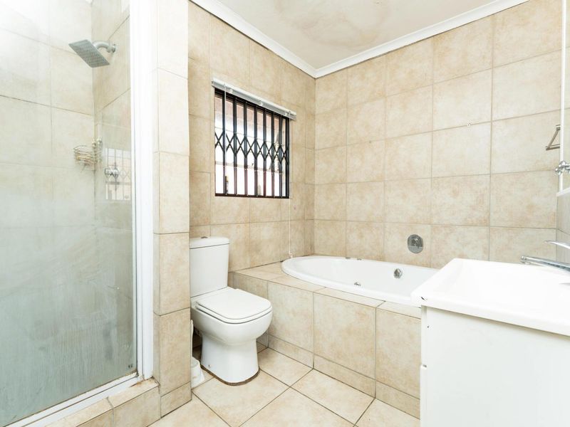 A functional bathroom featuring a built-in bathtub, separate shower enclosure, toilet, and vanity basin with neutral floor-to-ceiling tiling.