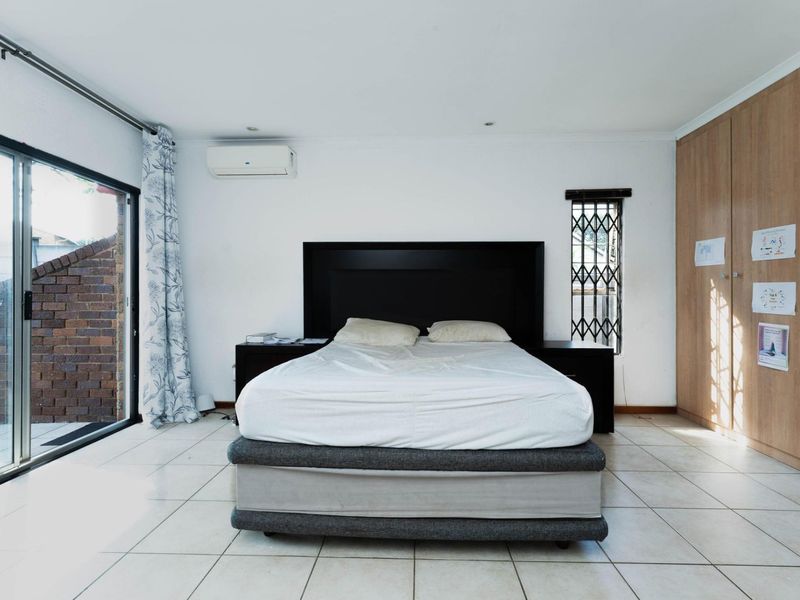 Spacious bedroom featuring tiled flooring, built-in cupboards, a split-system air conditioner, and a sliding glass door providing access to the exterior.