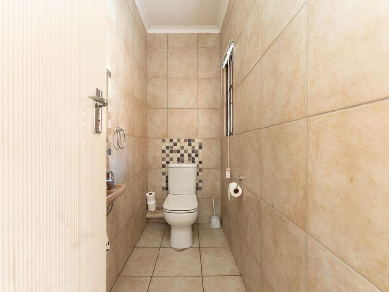 A compact guest bathroom featuring floor-to-ceiling ceramic tiling, a modern toilet, and a small wall-mounted basin with mosaic accent detailing.